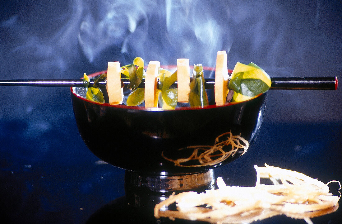 Schwarze Schale mit Miso-Suppe, die Zutaten sind auf Stäbchen augespießt