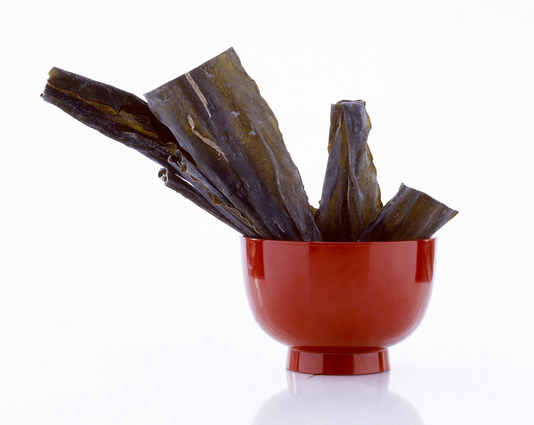 Algae leaves in a red pottery bowl against white background