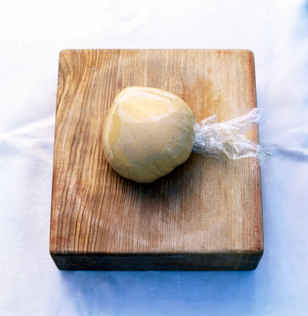 Pasta dough in plastic wrap on wooden board
