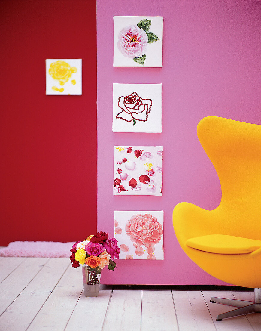 An einer Rose Wand hängen 4 Bilder mit Rosenmotiven,gelber Sessel