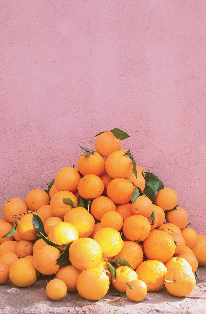 Ein Haufen Orangen in Form einer Pyramide vor rosa Wand