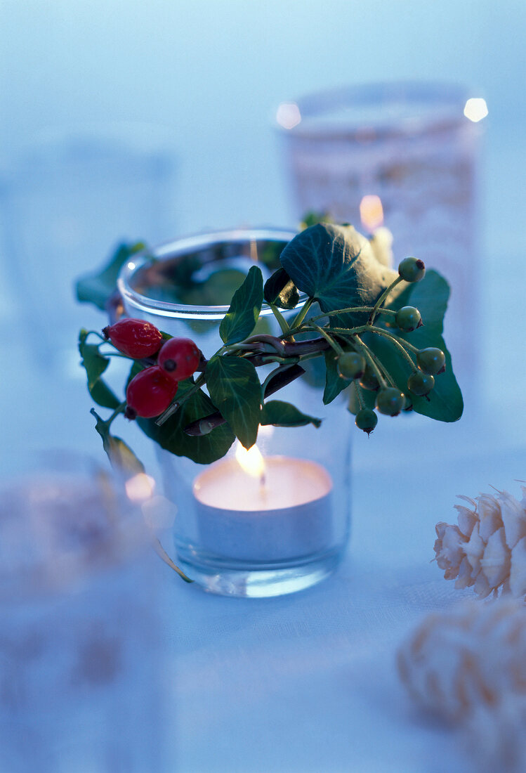 Lit candle in glass decorated with rose hips and berries