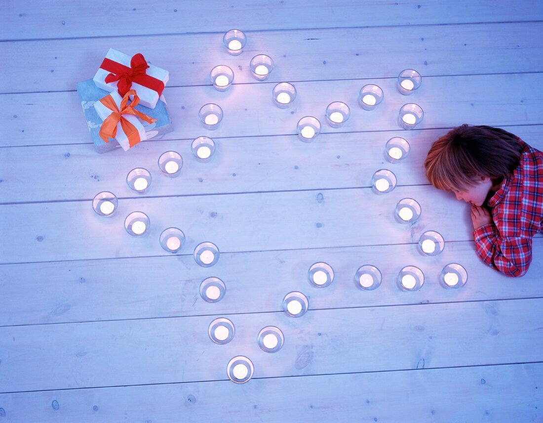 A child lying on floorboard beside tealights arranged in a star shape with presents next to it