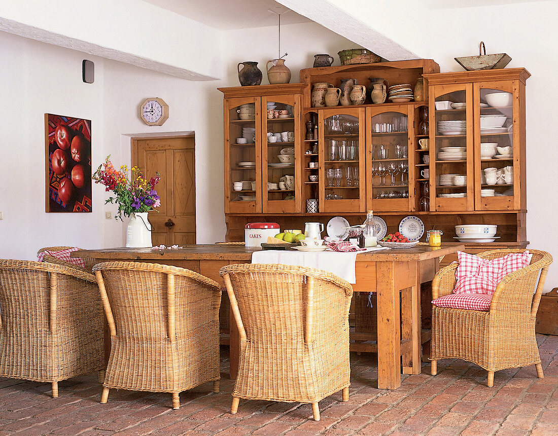 Farmhouse kitchen with buffet on wooden dining table and wicker armchairs