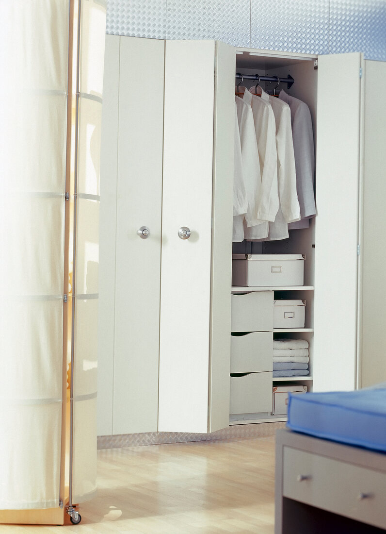 Clothes in white wall wardrobe with folding doors