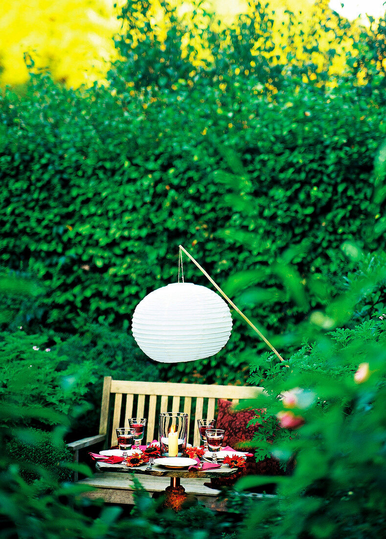 Table laid with lit candles and lantern in lush garden