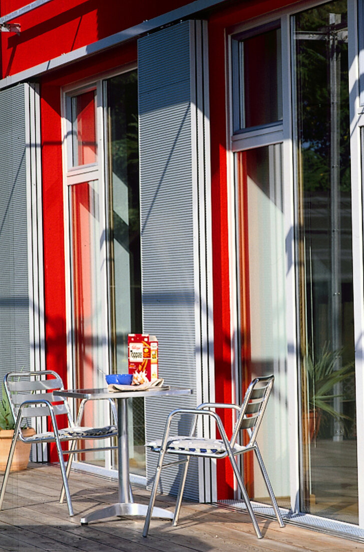 Bistrotisch mit Stühlen vor Fenstertüren mit Aluminiumläden