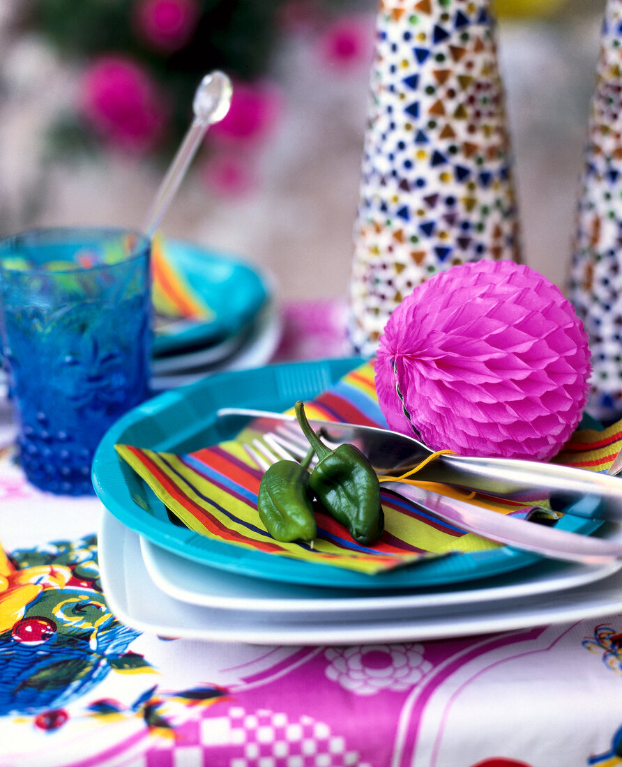 Close-up of pink paper ball with multi-coloured striped napkins on turquoise plastic plate
