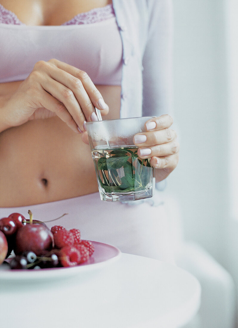 Frau in Wäsche mit einem  Glas mit Minze, Teller mit Obst, Früchte