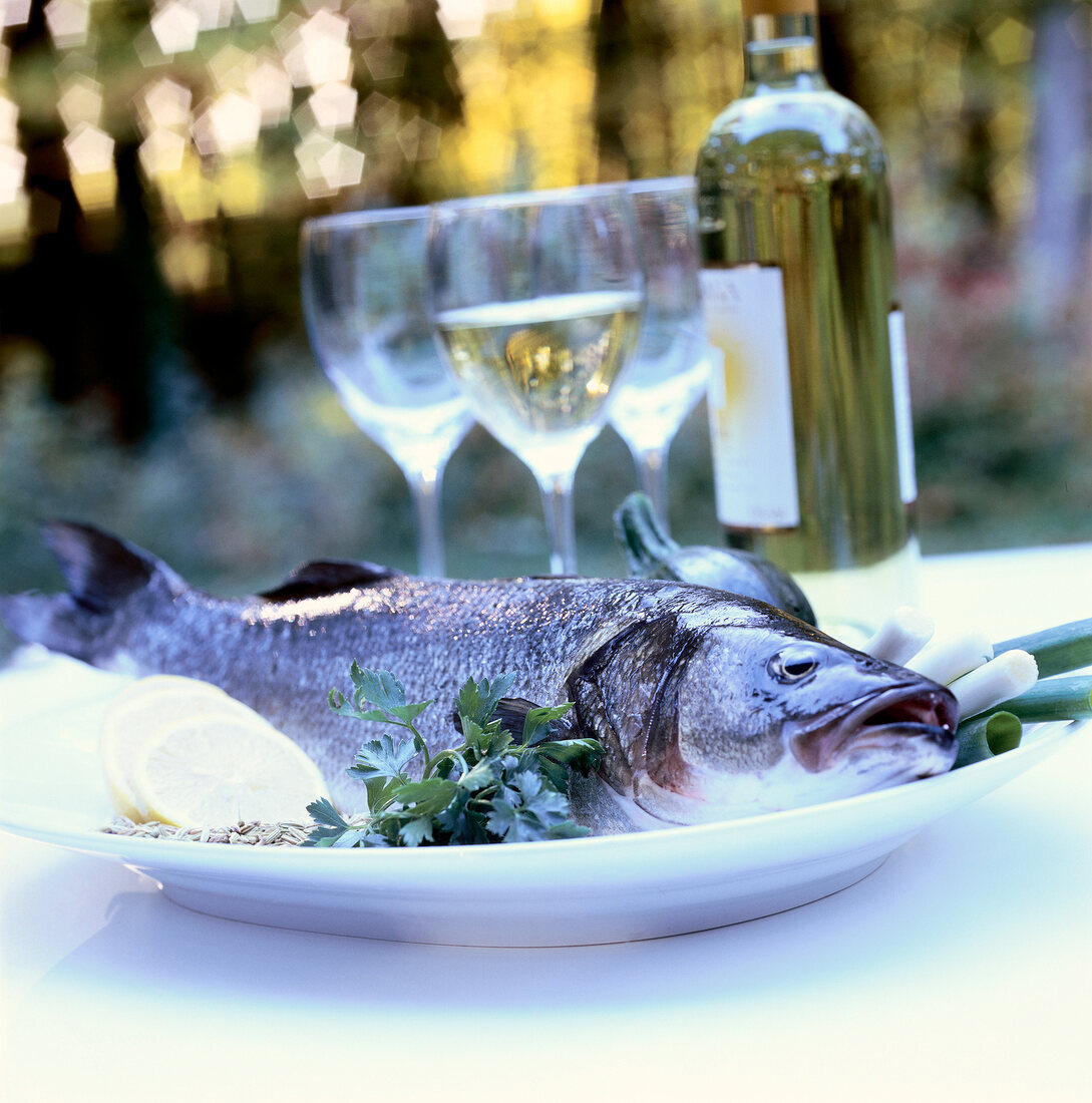 Close-up of fresh seabass on plate with lemon, herbs and spices