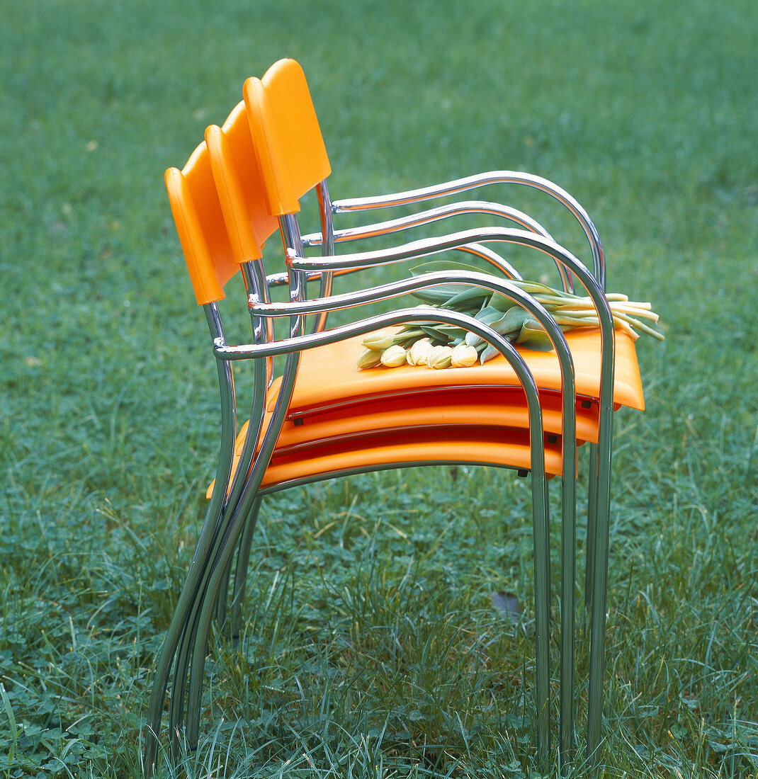 Stacked orange garden chairs with flowers in garden