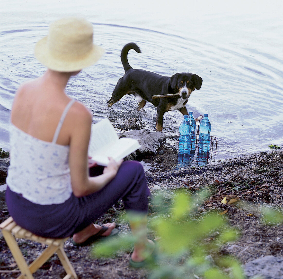 Frau mit Buch in der Hand am Ufer eines Sees sitzend