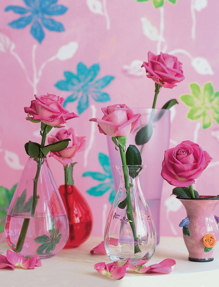 Flower vases with roses in front of flowered pink wallpaper