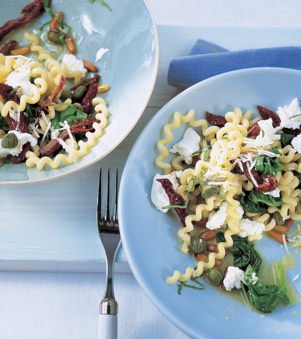 Fusilli mit Spinat, getrockneten Tomaten + Ricotta auf blauen Tellern