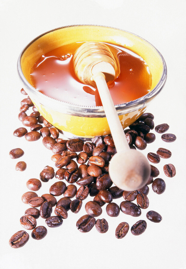 Coffee beans with honey and honey dipper in bowl