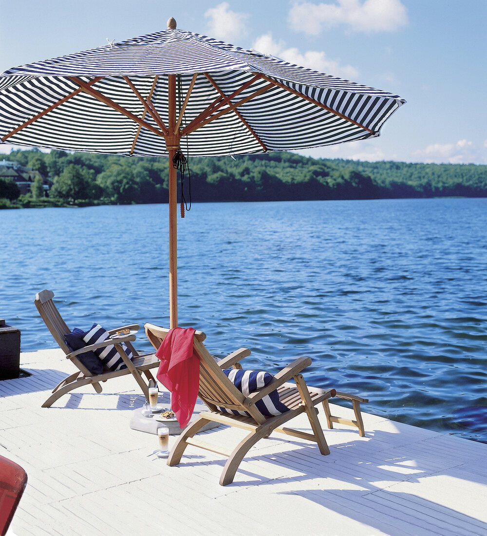 2 Deckchairs mit gestreiften Kissen auf Holzsteg mit Sonnenschirm am See