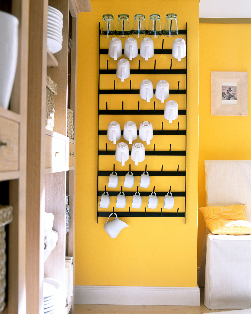 Crockery on hook board made of lacquered metal on yellow wall