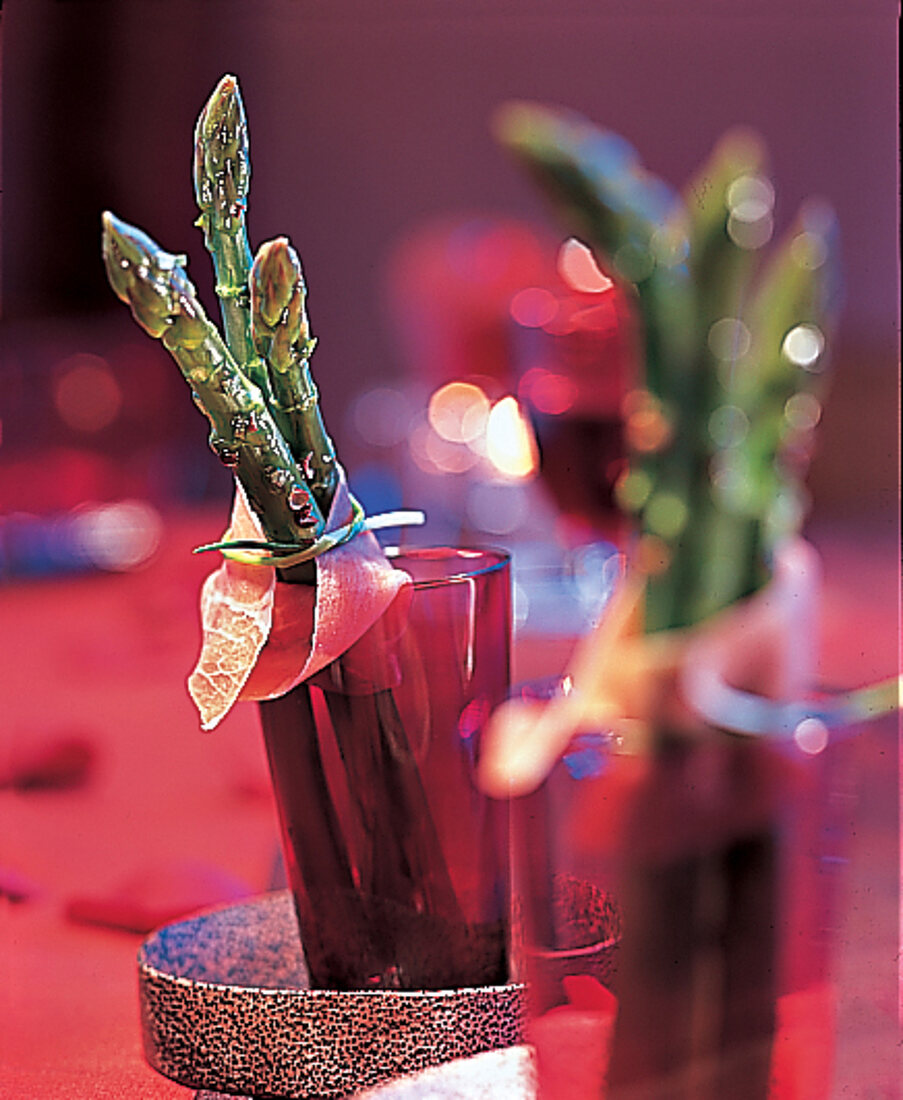 Amuse bouche: grüner Spargel mariniert, in roten Gläsern Kerzenschein