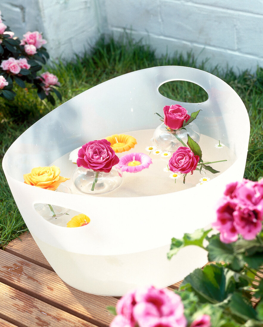 Transparent plastic water bucket with floating candles and flower heads