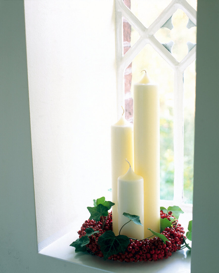 White altar candles with red berries and green ivy wreath on window