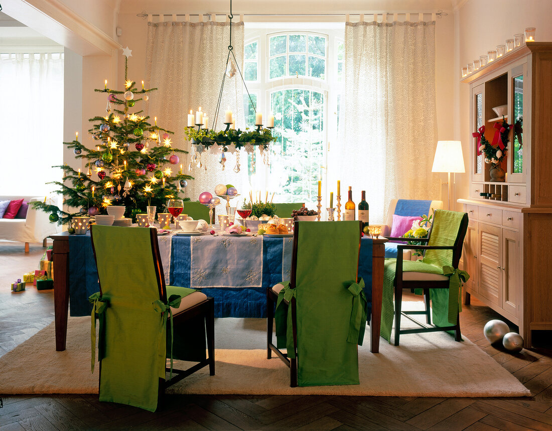 Decorated dining table with green slipcovers and Christmas tree on side