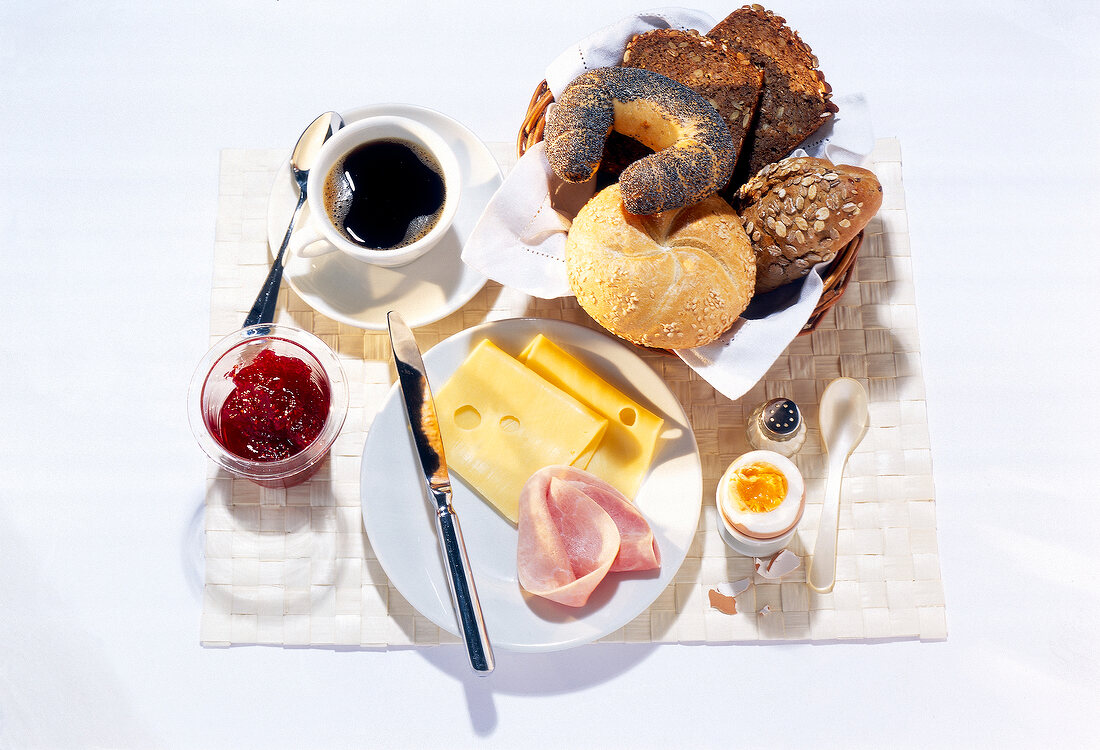 Breakfast table set with coffee, egg, cheese, ham, bread rolls, Marmelade on table mat