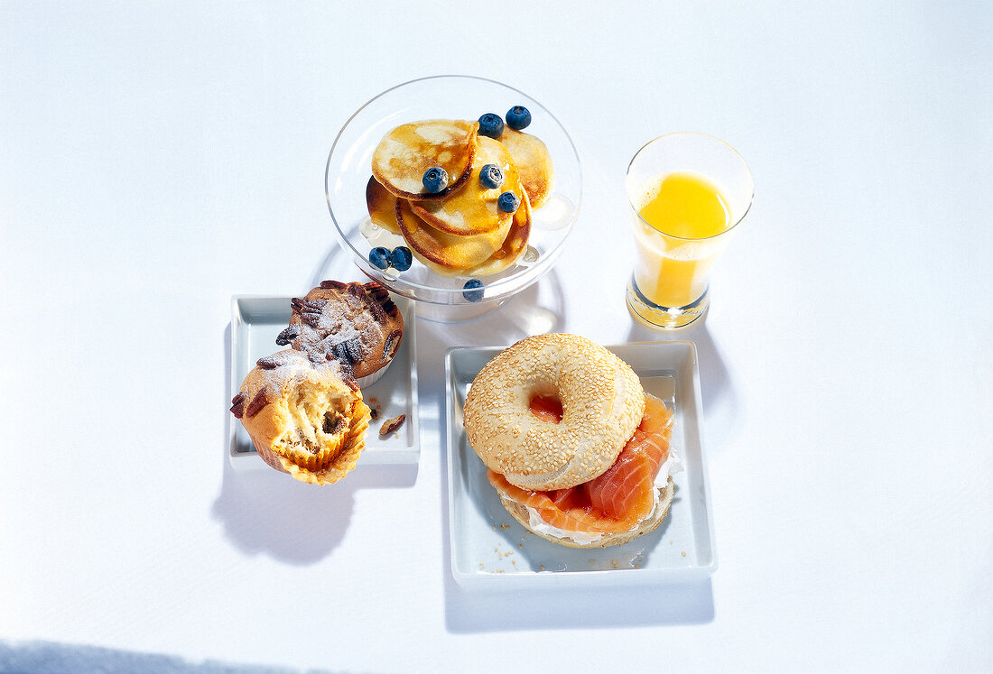 Breakfast table set with bagel, muffin, orange juice and pancakes on square plate