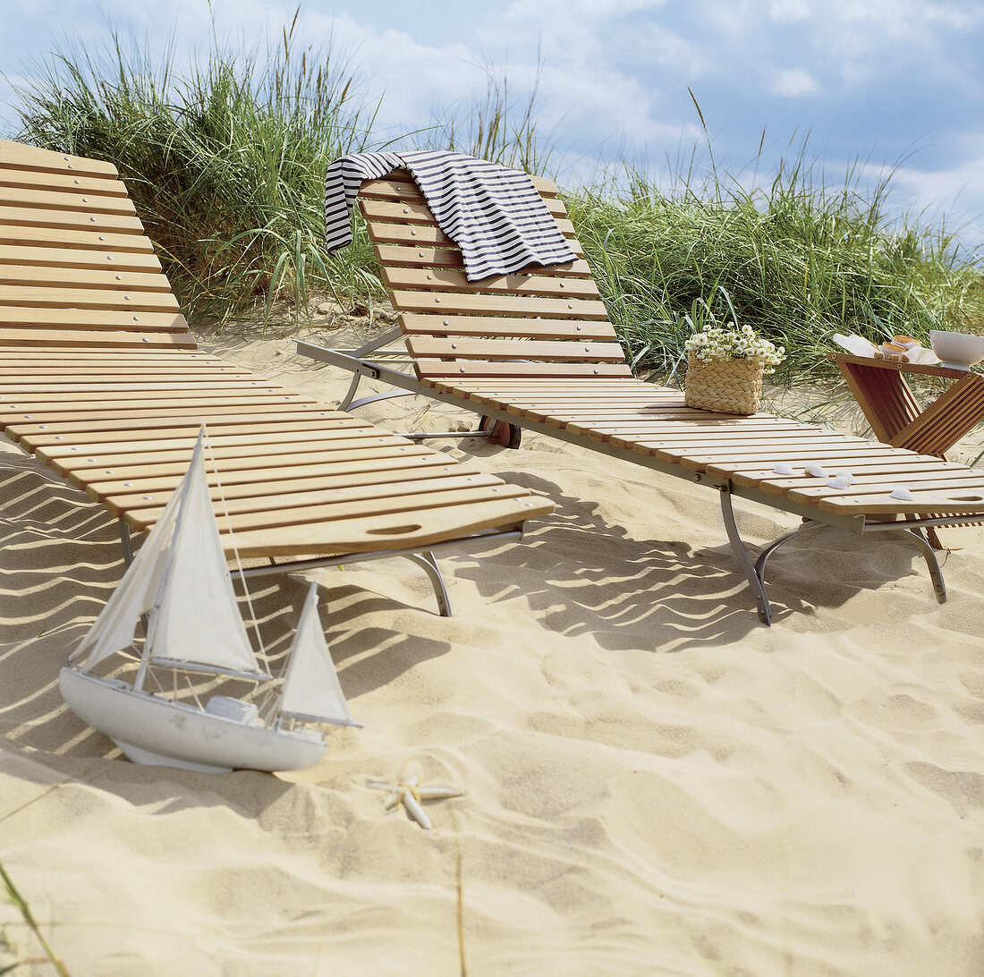 Two wooden deck chairs in sand dunes on the beach