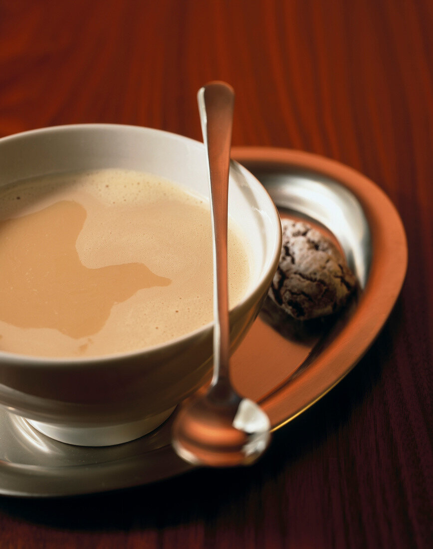 Cup of milk coffee on steel tray with a spoon