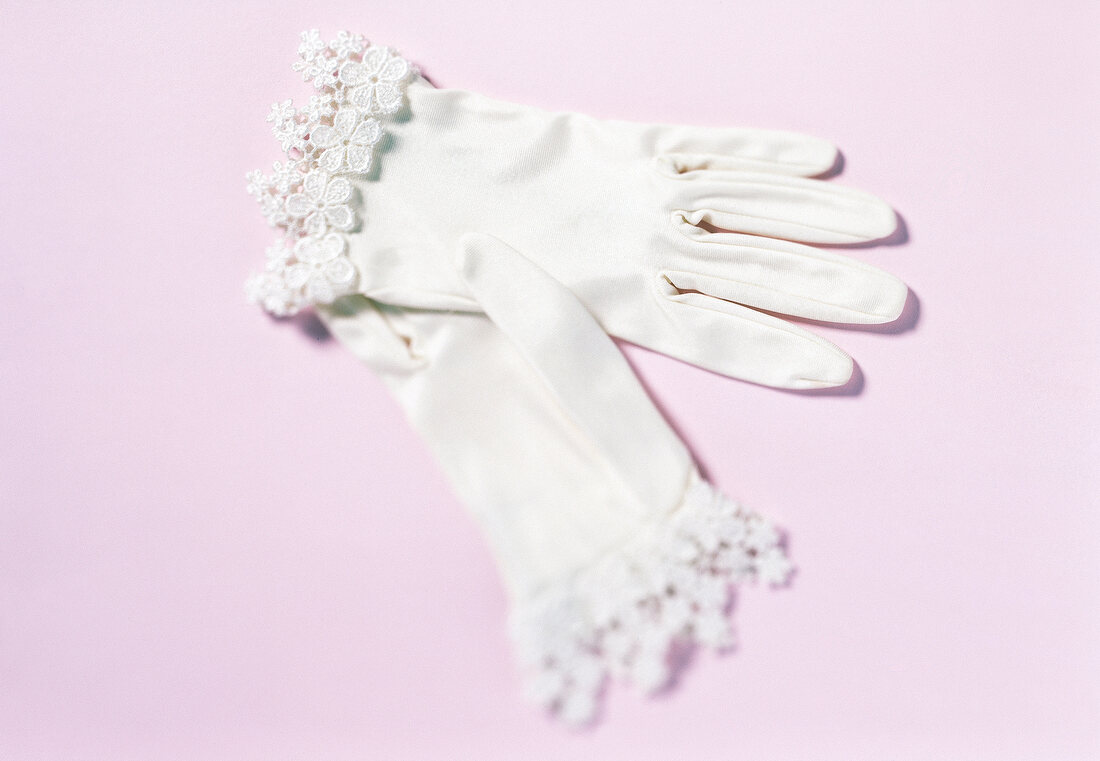 Close-up of white gloves with lace on pink background