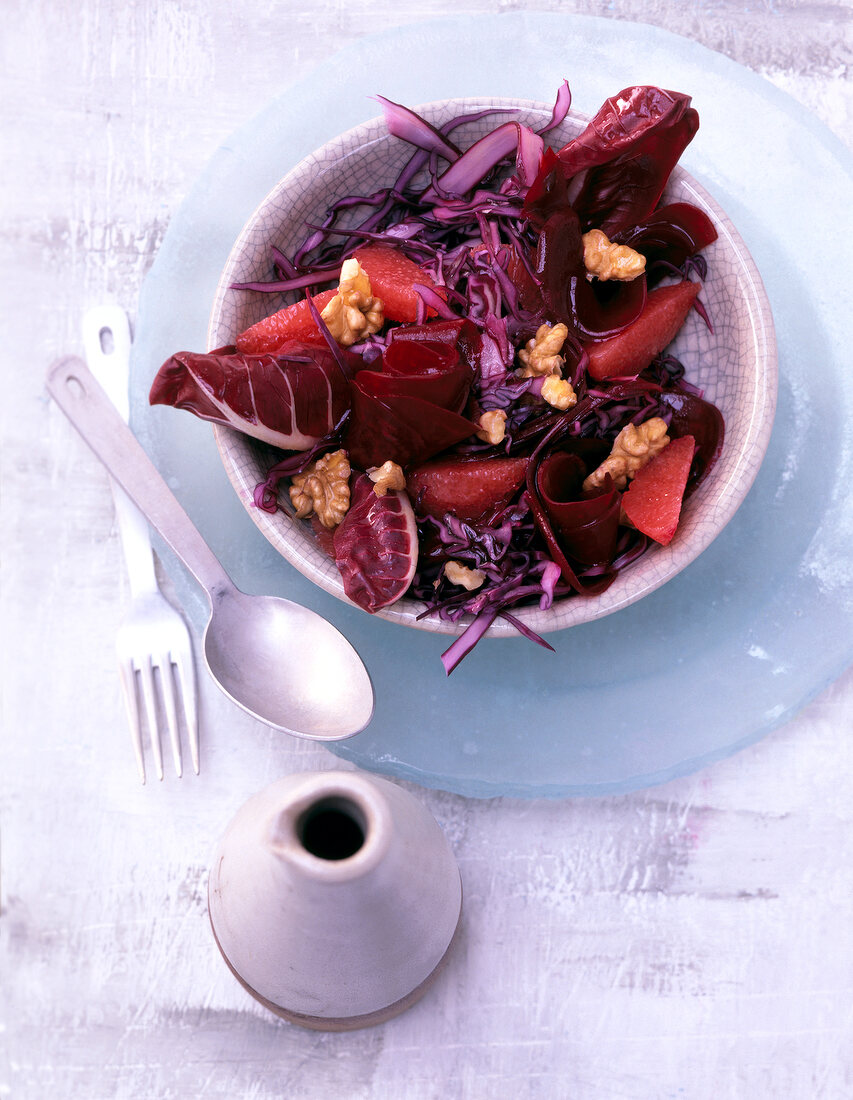 Red cabbage and walnut salad in a bowl on glass plate with fork and spoon