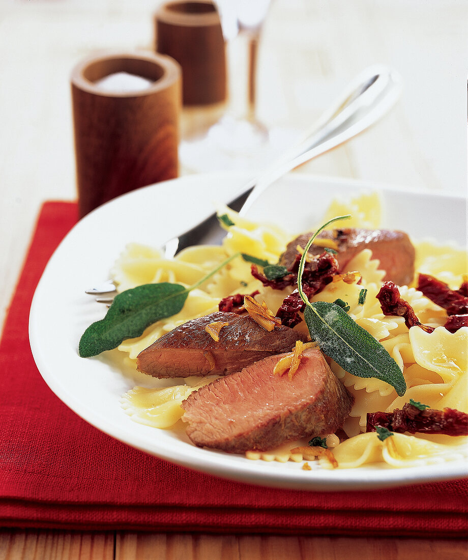 Farfalle pasta with lamb fillet, sage and butter on white plate