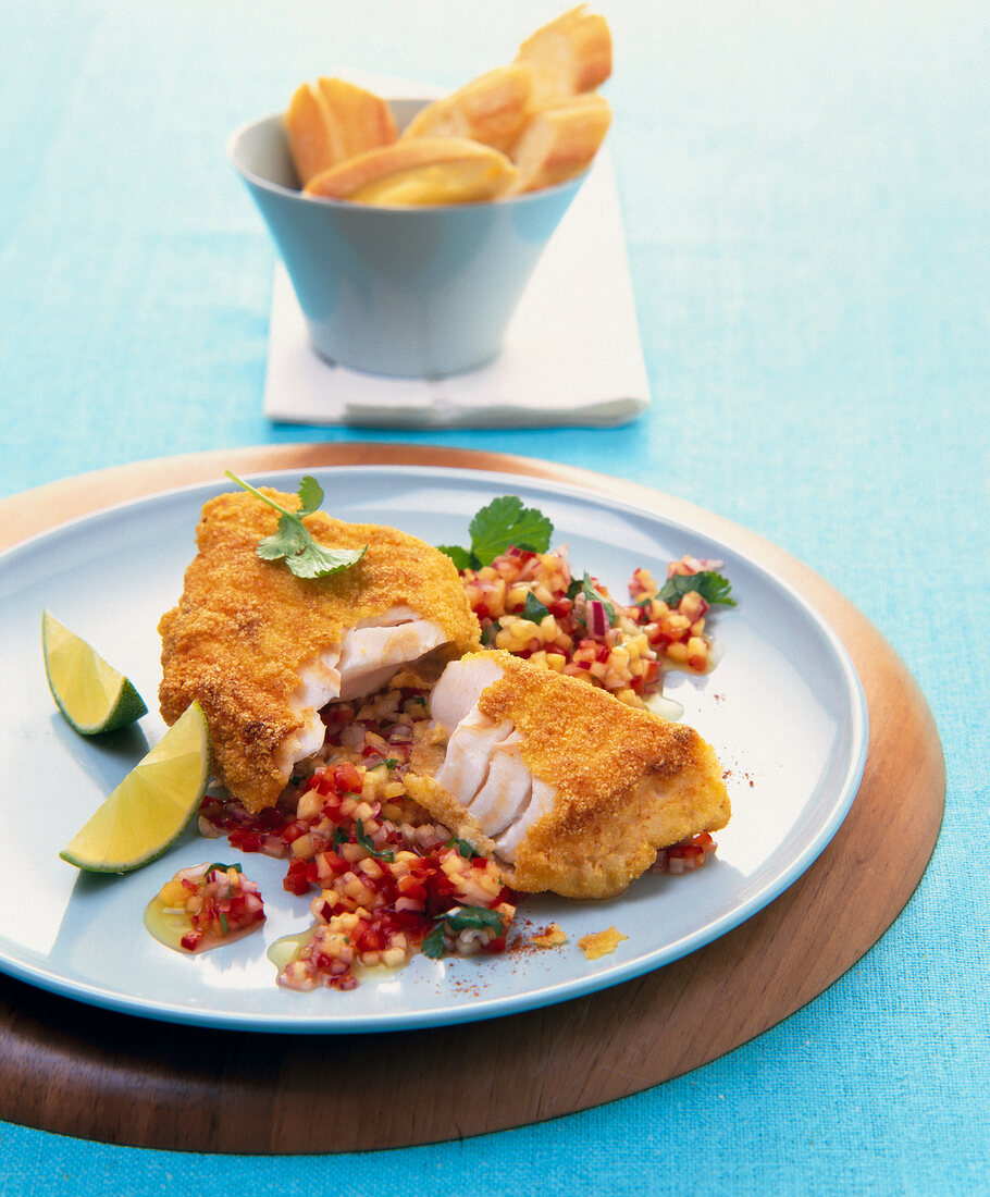 Fish with polenta crust, pineapple salsa and lemon wedges on plate