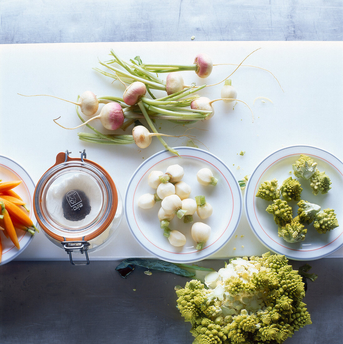 Carrots, turnips and romanesco florets on plates and truffle sauce in jar, overhead view