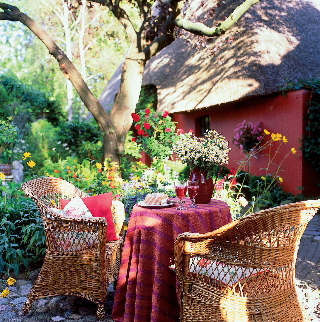 Table laid with wine and cakes with wicker chairs around on garden terrace