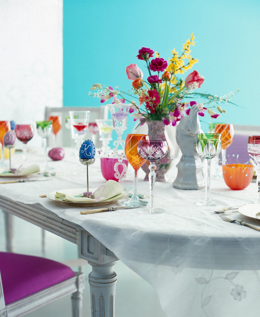 Table decorated with flowers, coloured glasses and Easter eggs in egg cup