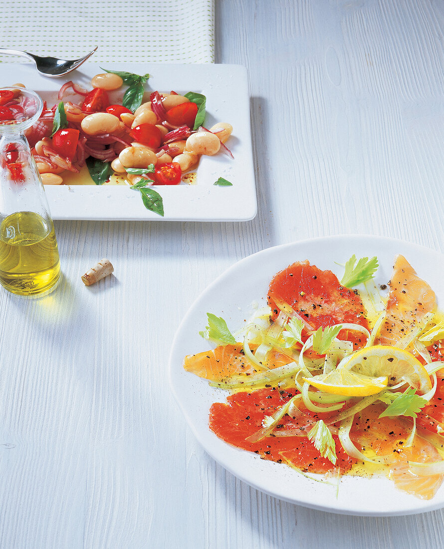 Fish carpaccio and thick white beans on plate with tomatoes on tray