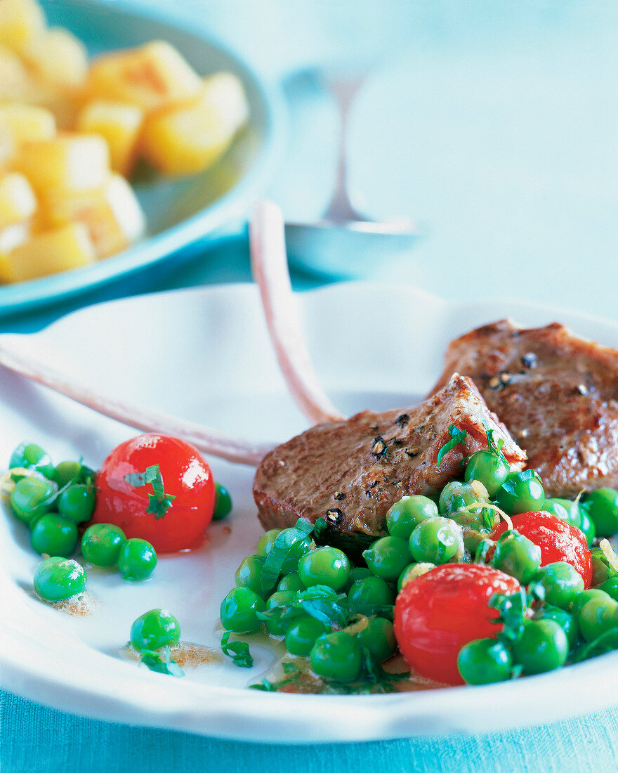 Close-up of lamb chops with green peas and cherry tomatoes on plate