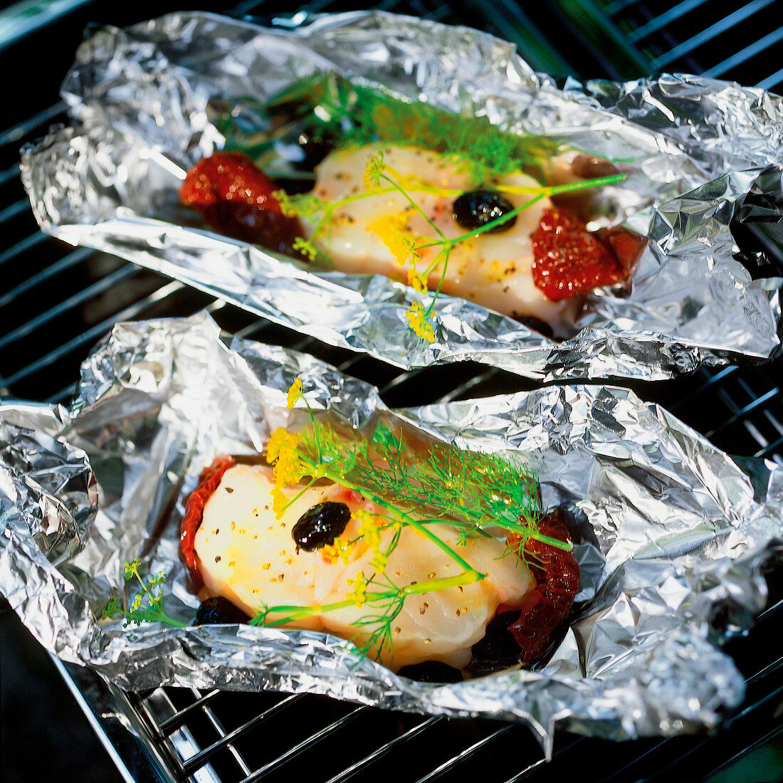 Monkfish with dried tomatoes and olive being grilled in silver foil