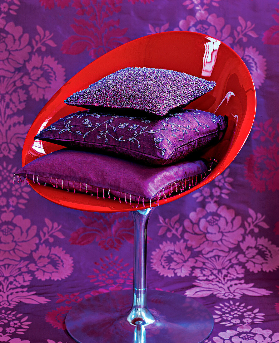 Stack of purple satin and silk cushions on red shell chair
