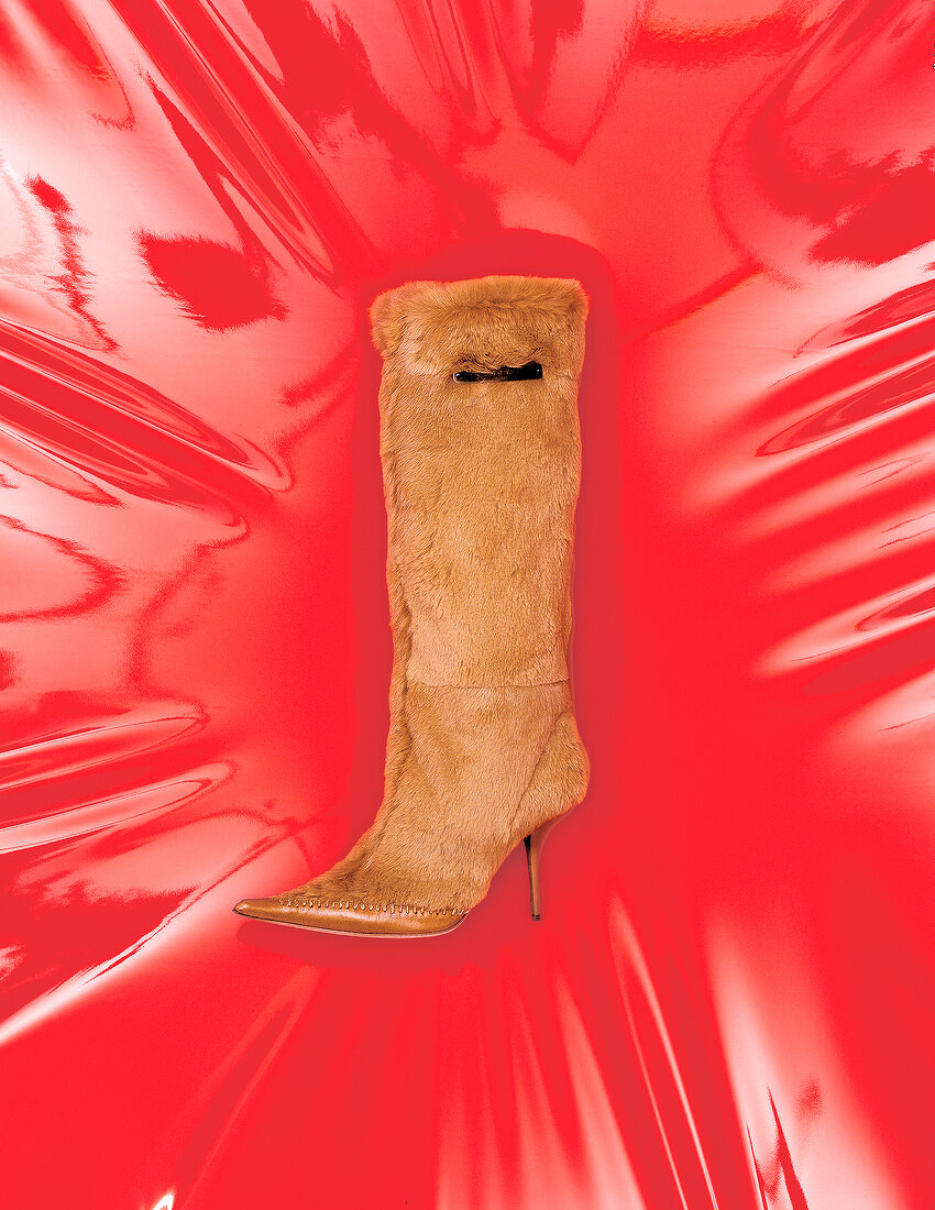 High heeled brown fur and leather knee length boot on red background