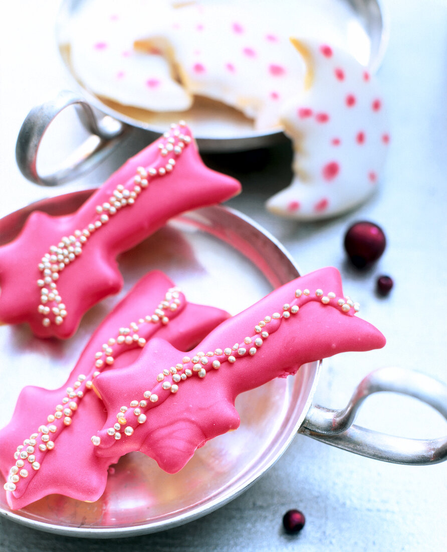 Close-up of butter biscuits decorated with pink icing and pearls on steel plate