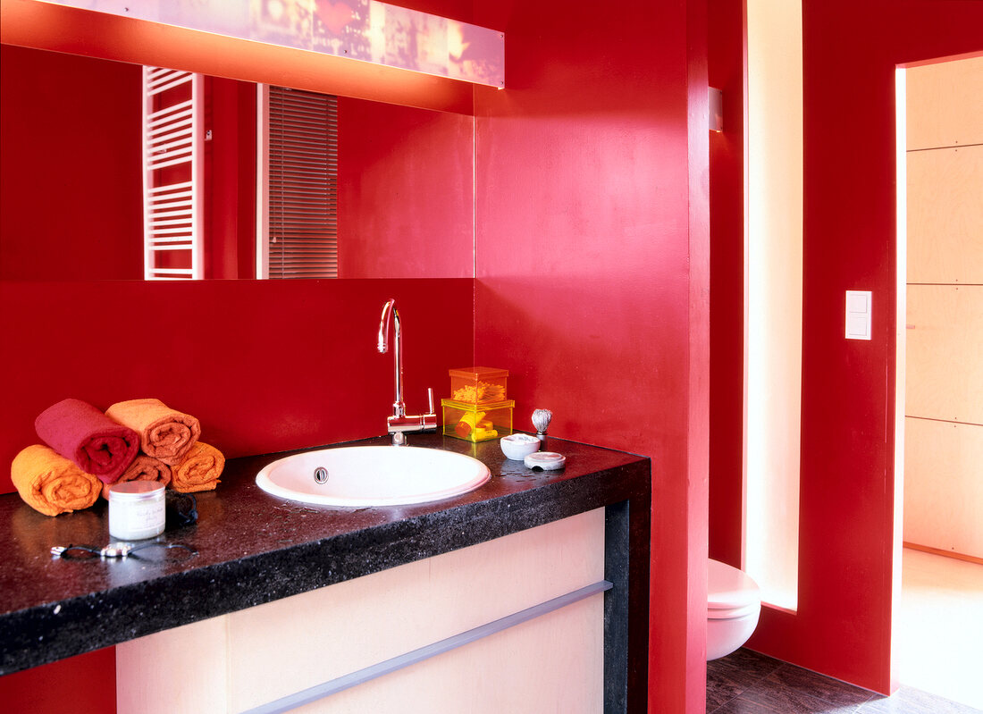 Interior of bathroom with white toilet seat, wash basin and red walls