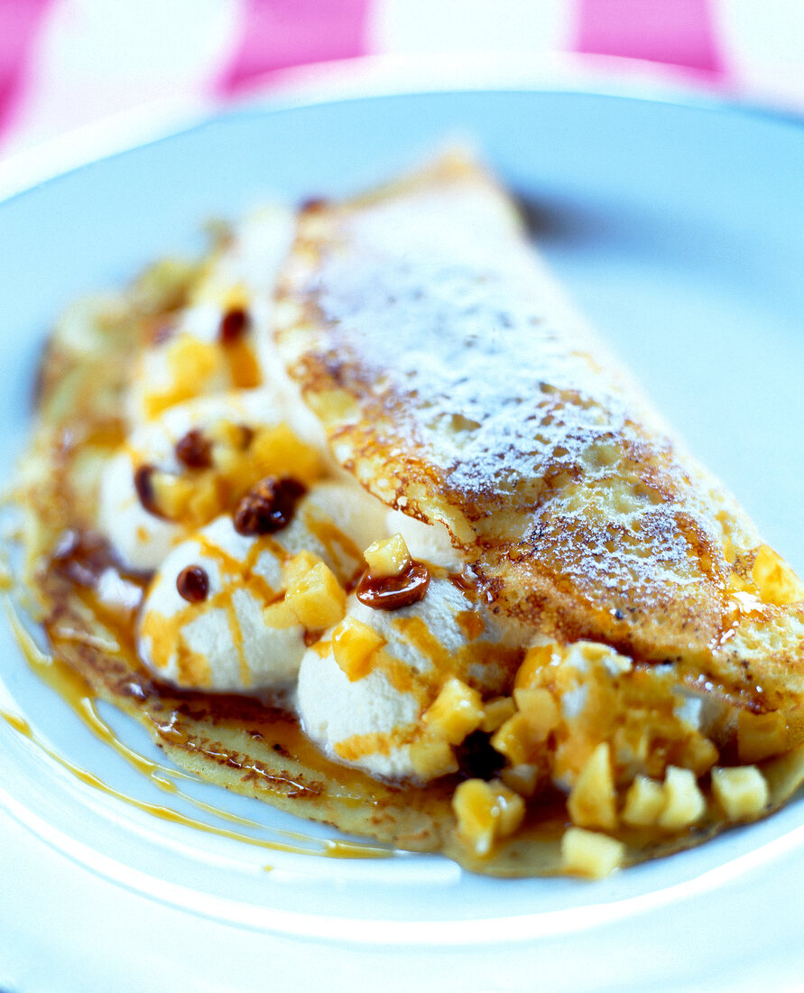 Close-up of pancake with caramel, cream and quince pieces on plate