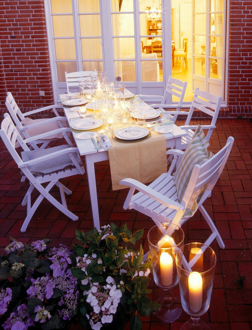 Laid dinning table with white chairs and lit candles on terrace