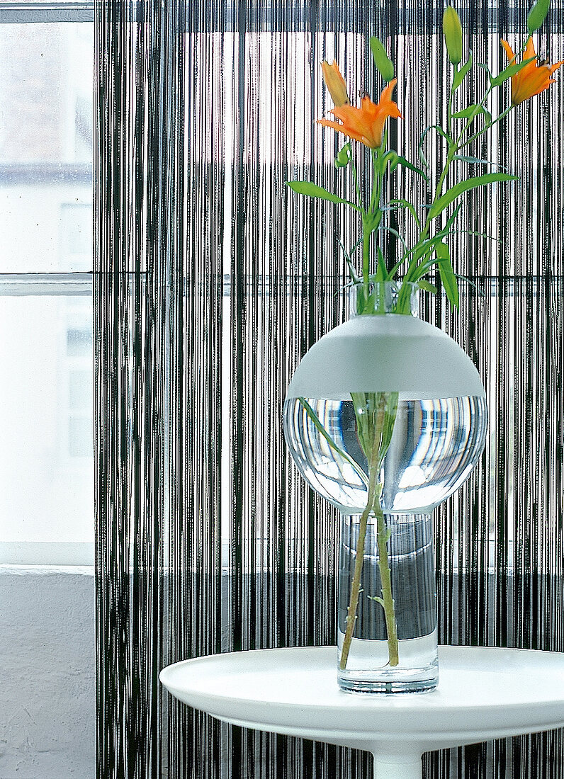Fadenvorhang aus Fäden vor Fenster, Vase mit Blumen auf Beistelltisch