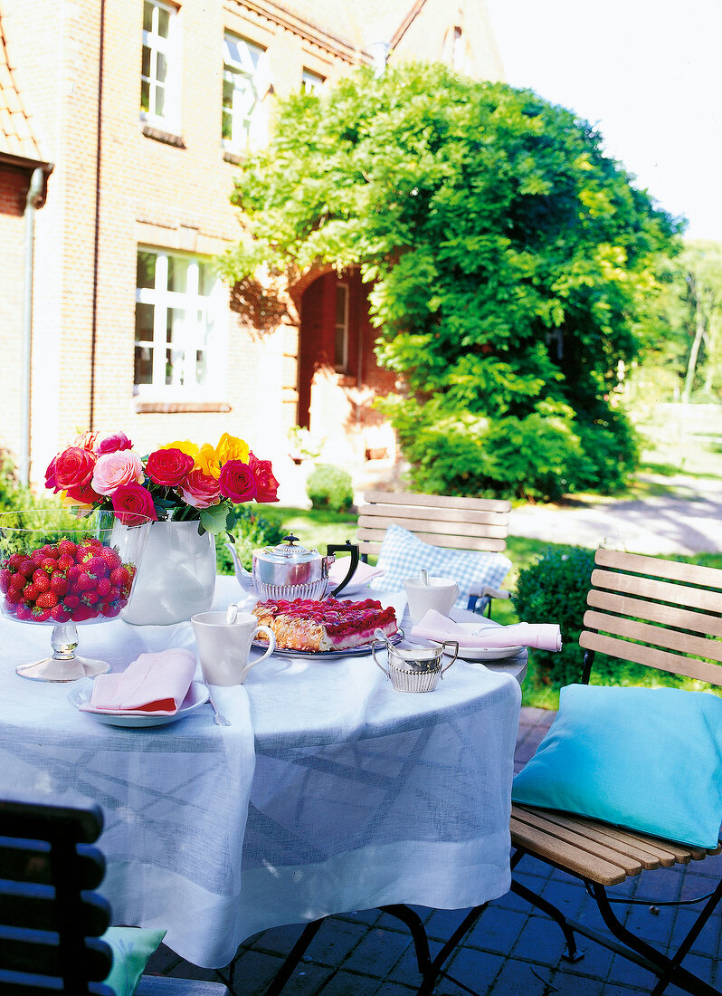 Breakfast table laid with cake, coffee and flowers in garden