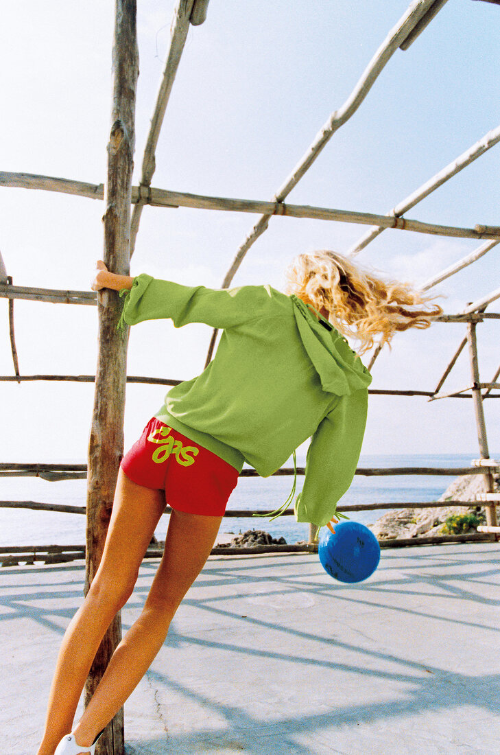 Frau spielt mit Ball, sportlich bunt gekleidet, sommerlich, Rückenansicht