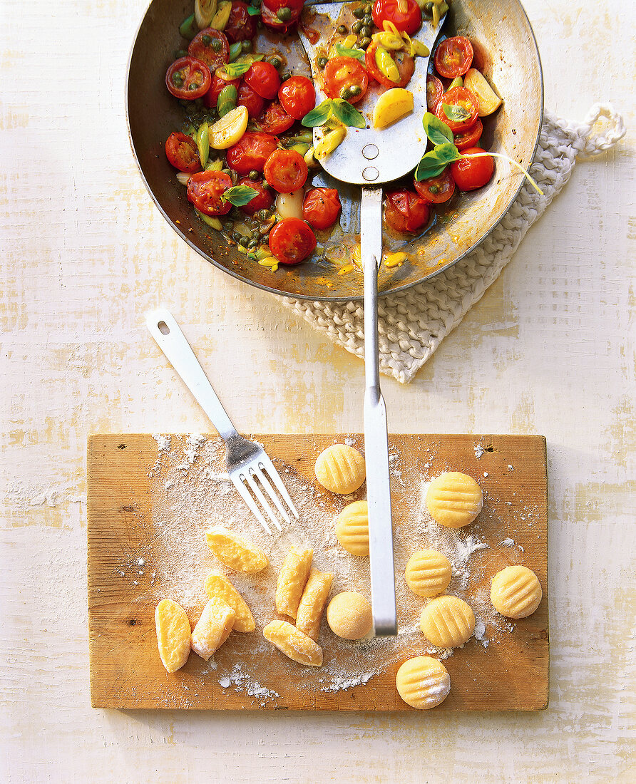 Italian pasta in wok beside potato gnocchi on wooden board