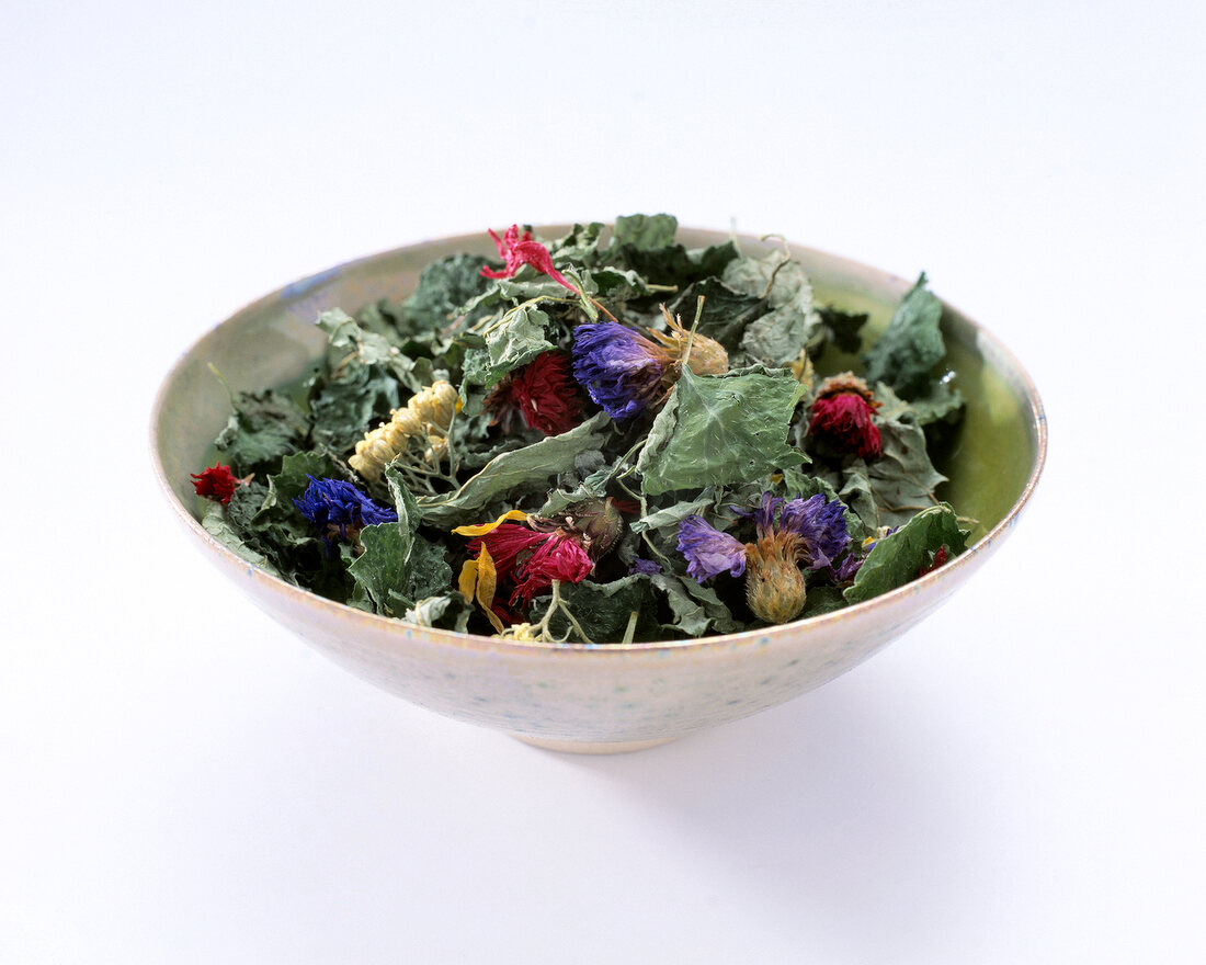 Bowl with dried flowers and herbs on white background